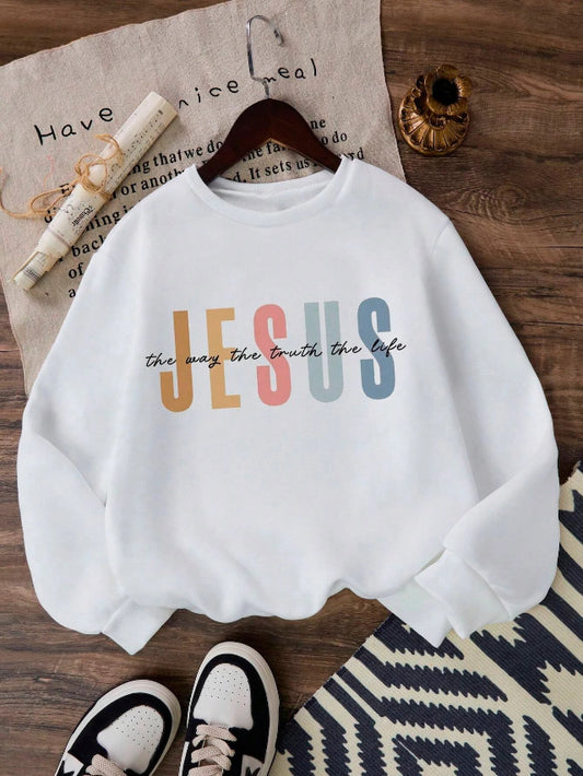 White sweatshirt with colorful 'JESUS' text on a wooden surface with shoes and a hanger.