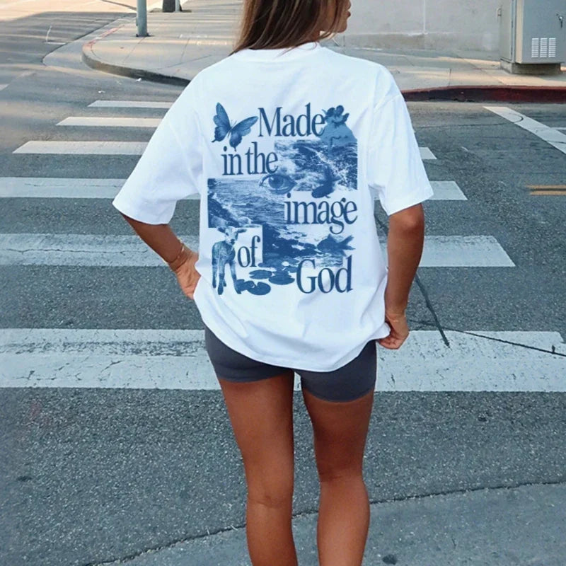 Person wearing a white t-shirt with blue text and graphics on the back, standing on a street.