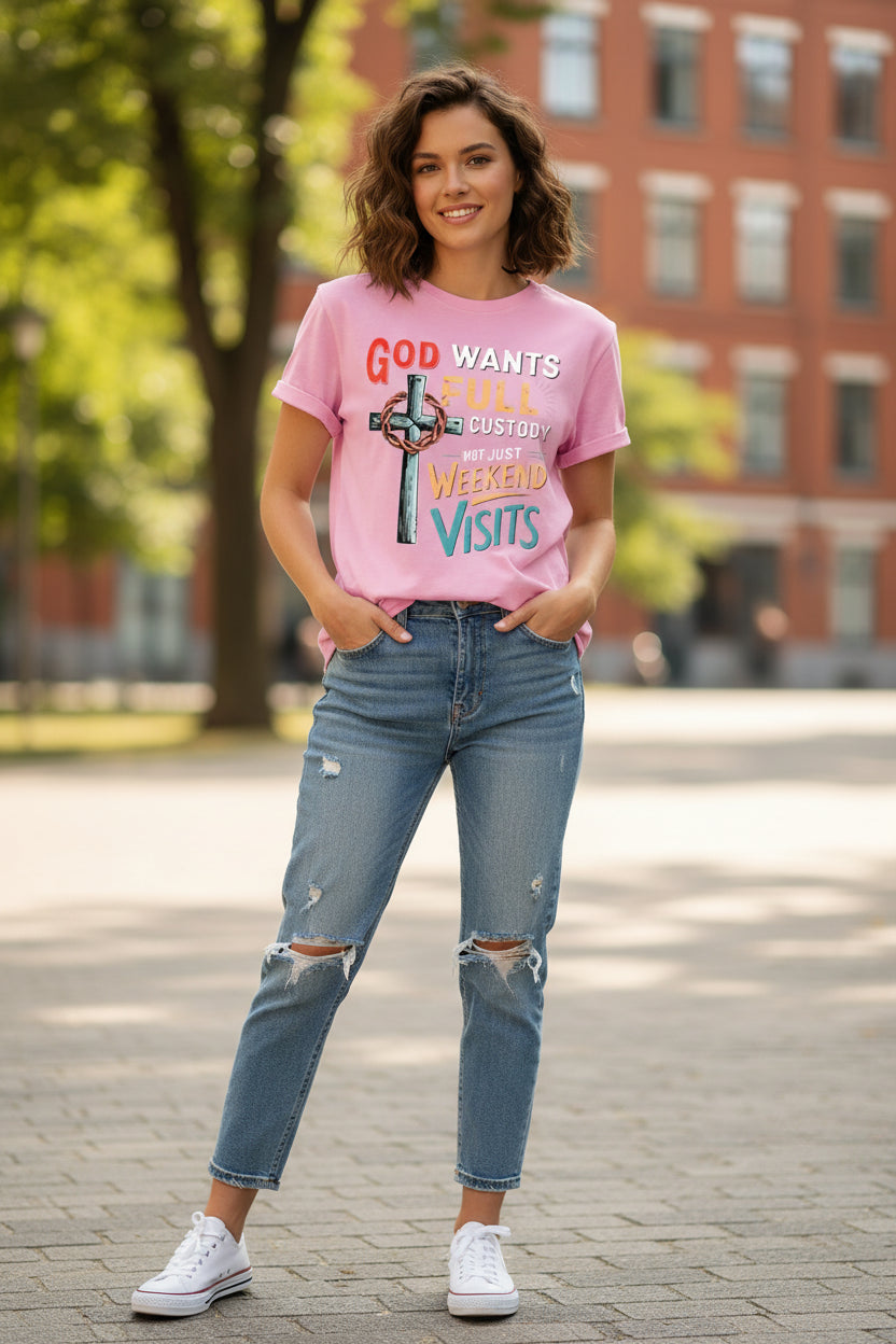 A light pink short-sleeve t-shirt with a colorful graphic print on the front. The graphic features a metallic-textured cross with a crown of thorns and the text 'GOD WANTS FULL CUSTODY NOT JUST WEEKEND VISITS' in red, white, yellow, and blue lettering.