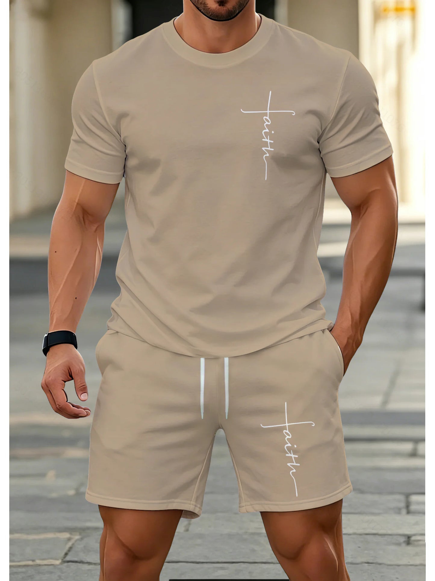 A man wearing a beige short-sleeve t-shirt and matching shorts set, both featuring a white cursive 'faith' graphic on the chest and thigh, standing outdoors on a paved walkway.