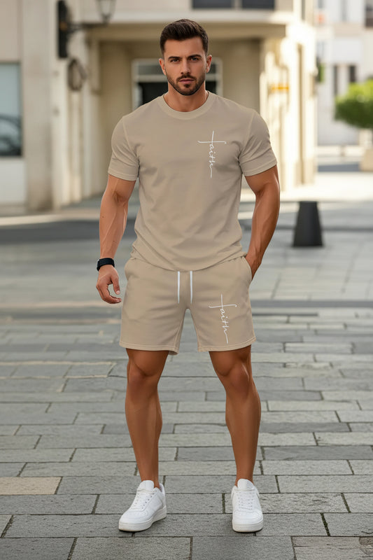 A man wearing a beige short-sleeve t-shirt and matching shorts set, both featuring a white cursive 'faith' graphic on the chest and thigh, standing outdoors on a paved walkway.