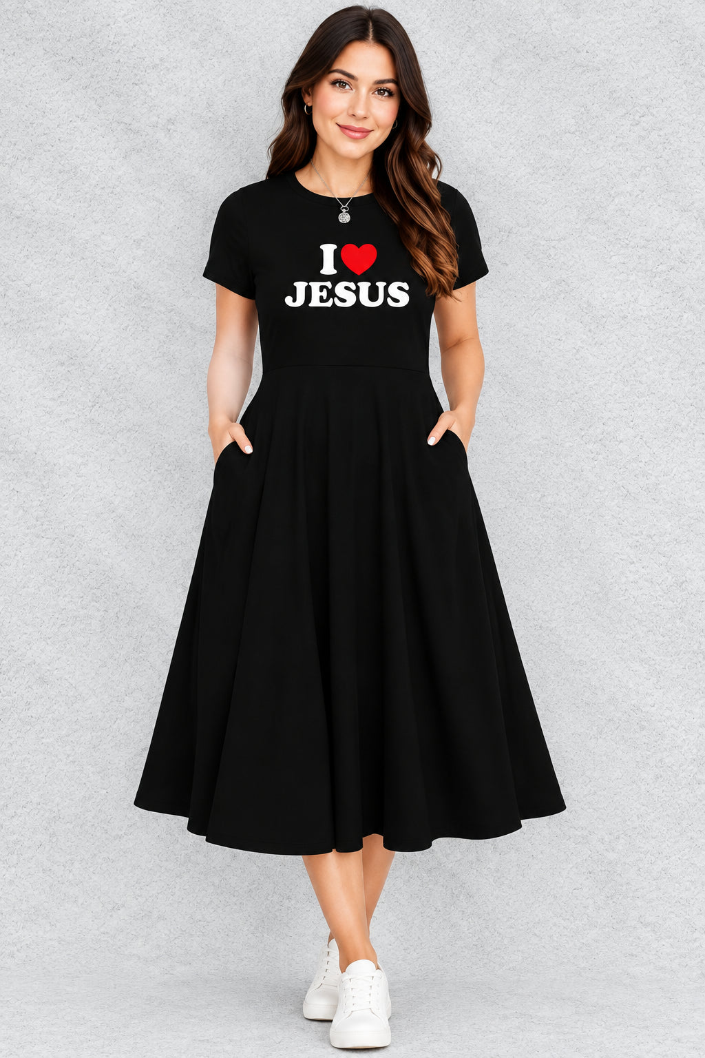 A woman wearing a black short-sleeve A-line dress with 'I [red heart] JESUS' printed in white and red on the chest, set against a textured gray background.