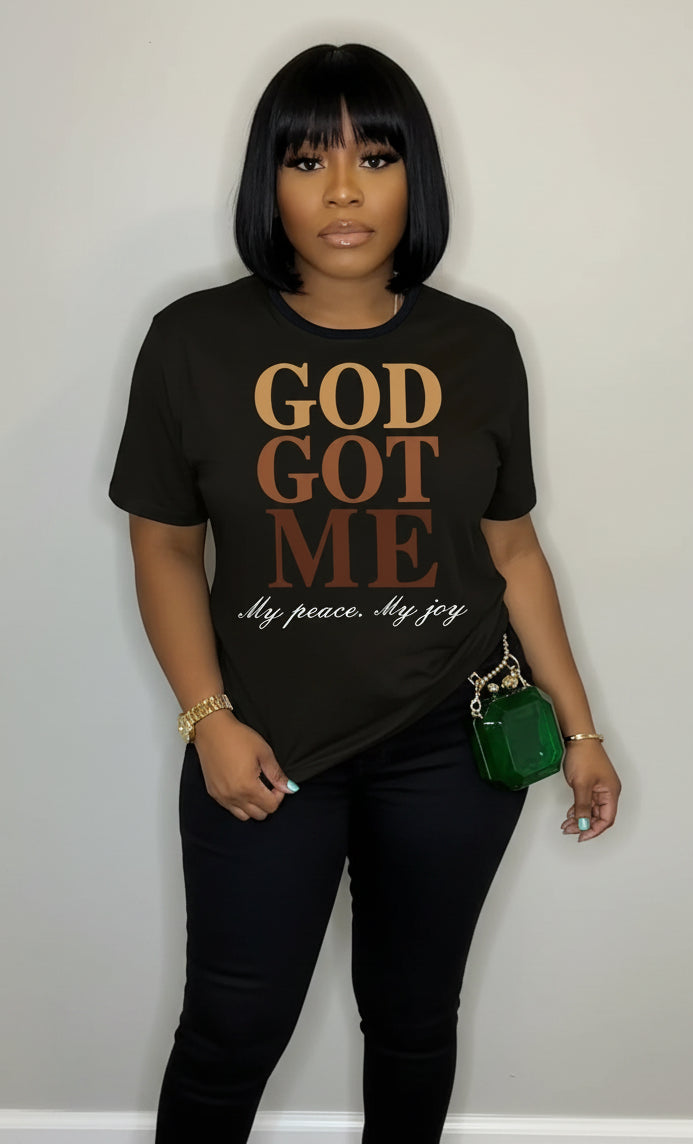 Person wearing a black t-shirt with 'GOD GOT ME' text, holding a green handbag.