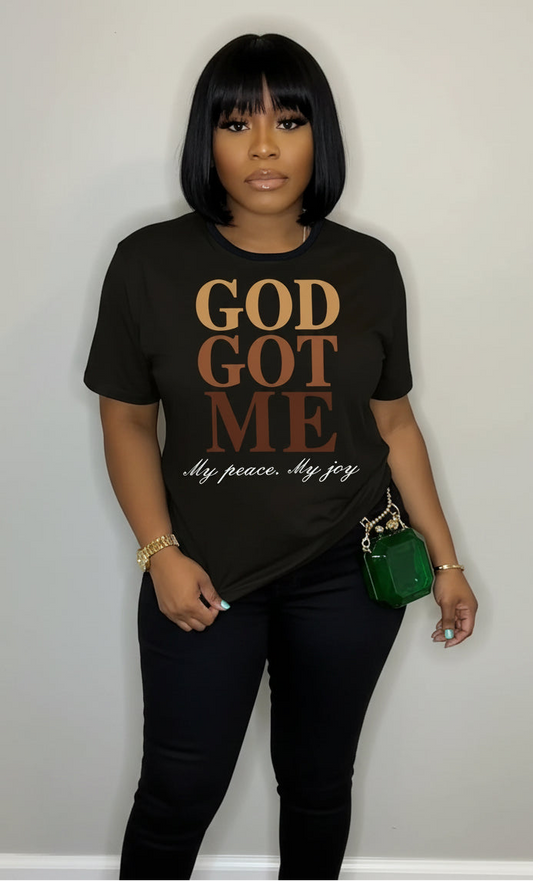 Person wearing a black t-shirt with 'GOD GOT ME' text, holding a green handbag.