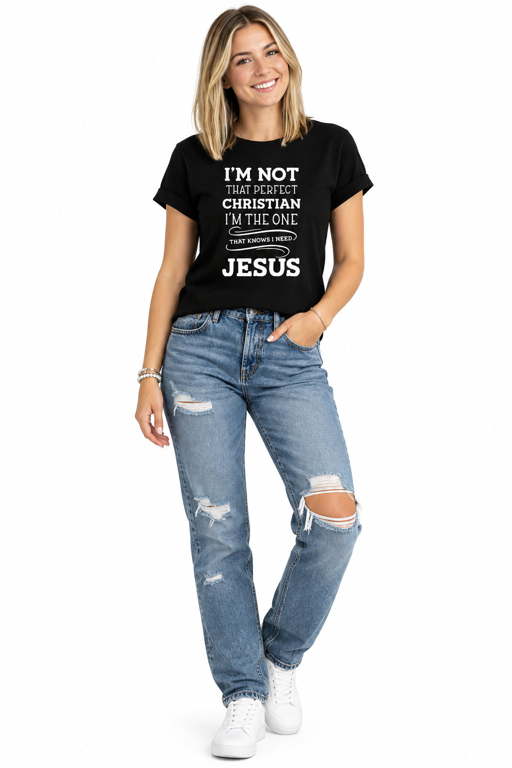 A woman wearing a black short-sleeve graphic T-shirt with white text that reads, 'I'M NOT THAT PERFECT CHRISTIAN I'M THE ONE THAT KNOWS I NEED JESUS,' paired with blue jeans against a plain white background.