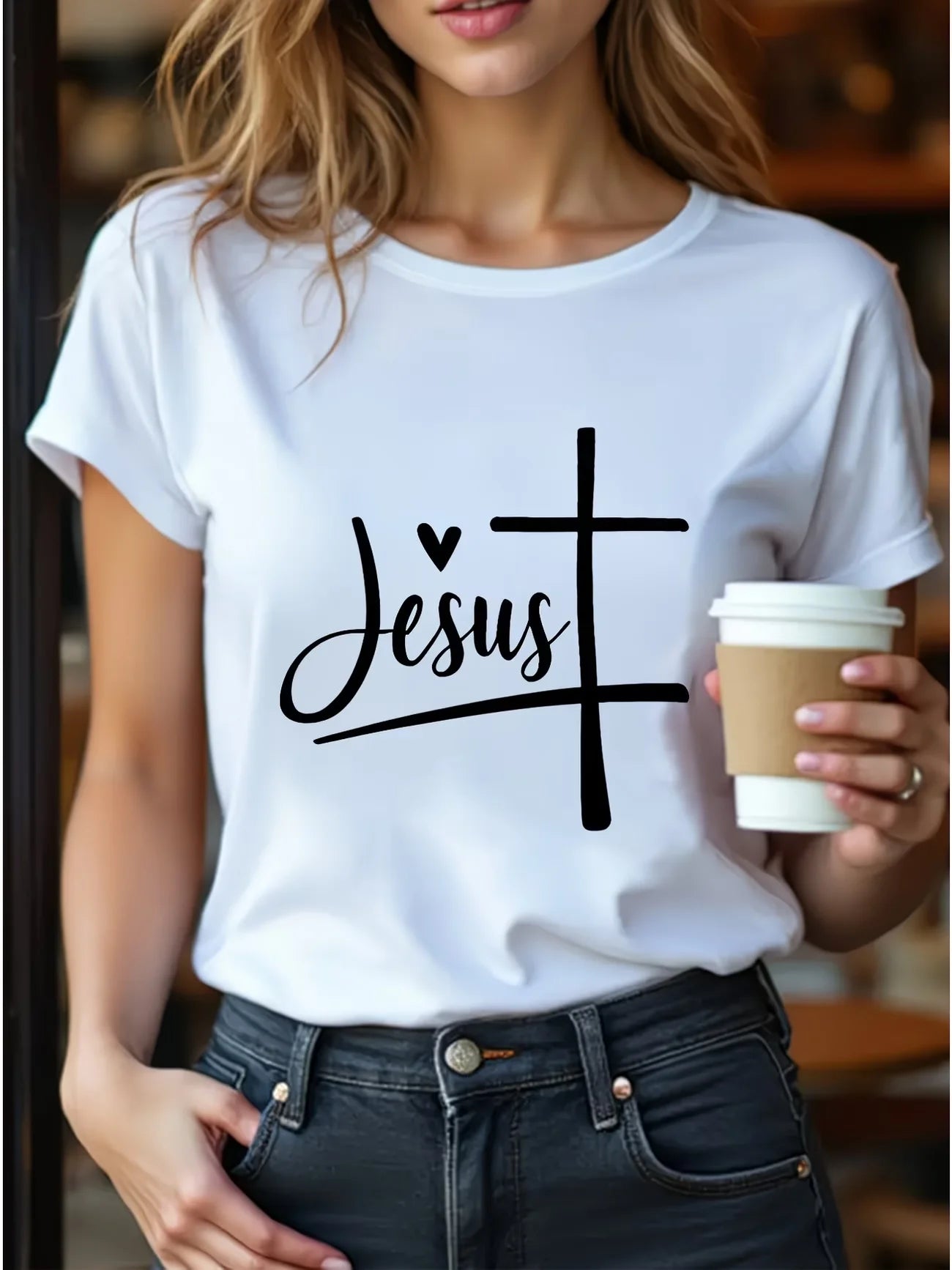 Person wearing a white t-shirt with 'Jesus' design, holding a coffee cup.
