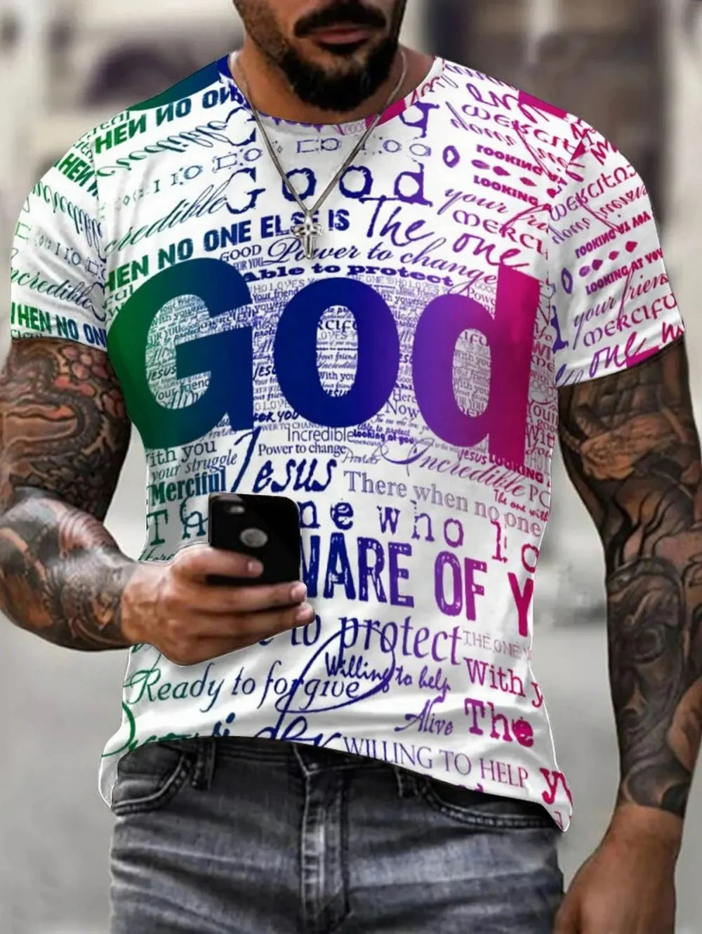 A man wearing a white graphic t-shirt with colorful text and the word 'God' in large gradient letters across the front, paired with gray jeans.