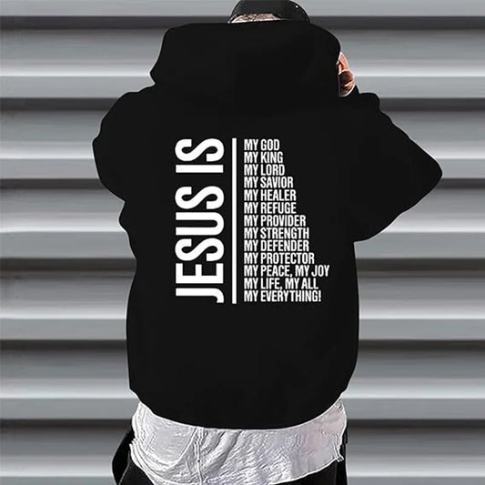 A person wearing a black hoodie with text 'JESUS IS' followed by various attributes of God in white letters on the back of the hoodie.
